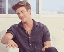 a man in a blue shirt is sitting on a white couch and smiling .