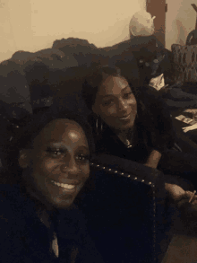 two women are sitting on a couch and smiling