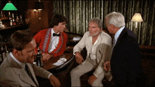 a man in a red jacket sits at a bar talking to three other men