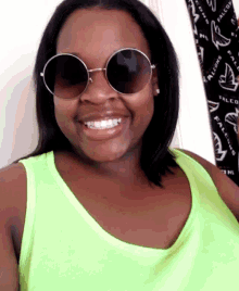 a woman wearing sunglasses and a neon green tank top smiles for the camera