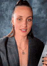 a woman wearing a necklace with a coin on it is smiling