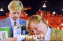 a man holding a box of brake pads and another man holding a cell phone says " what "