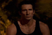 a man in a black tank top looks at the camera with a serious look on his face
