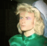 a close up of a person 's face with blonde hair and a green shirt