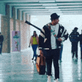 a man walking down a hallway carrying a guitar and a backpack with the letter r on his jacket