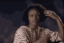 a woman in a striped shirt is holding her hair in a ponytail .