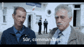 two men are standing in front of a building that says " sur , commandant "
