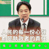 a man in a suit and tie is speaking into a microphone in front of a green sign