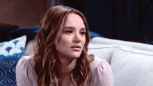 a woman in a pink shirt is sitting on a couch looking at the camera .