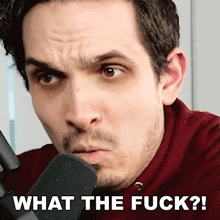 a man is talking into a microphone and making a funny face with the words what the fuck written on the bottom .
