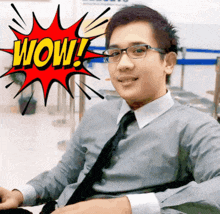 a man wearing glasses and a tie is sitting in front of a cartoon explosion that says wow