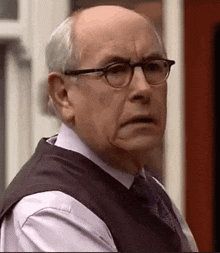 an elderly man wearing glasses and a vest is making a funny face