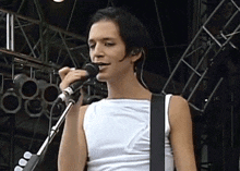 a man in a white tank top is singing into a microphone while playing a guitar .