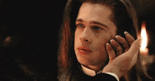 a man with long hair is wearing a tuxedo and touching his face .