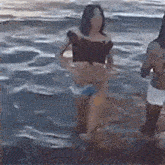 a woman in a bikini is standing in the water on the beach .