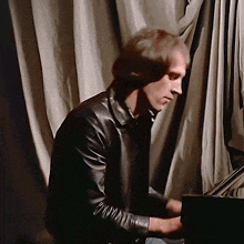 a man in a black leather jacket playing a piano