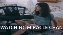 a man with long hair sits in front of a laptop with the words " watching miracle chan " on the bottom