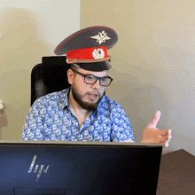a man wearing a military hat and glasses sits in front of an hp computer