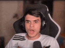 a man wearing headphones and a white shirt is sitting in a gaming chair .