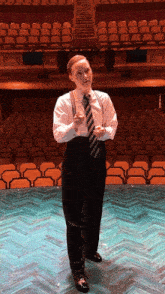 a man in a suit and tie stands on a stage in front of an empty auditorium