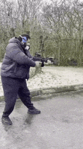 a man in a black jacket is holding a rifle on a street .