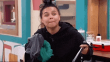 a woman wearing a black hoodie and green gloves is holding a pair of socks and a towel .