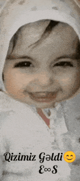 a baby wearing a white hat and a white jacket with the words " qizim geldi " on the bottom right