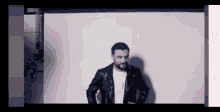 a man in a leather jacket stands in front of a white wall