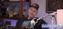 a man wearing a hat is sitting in front of a microphone with the words dark web behind him .