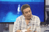 a man in a plaid shirt is sitting in front of a tv screen that says obras 11