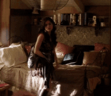 a woman sits on a bed in a room with a shelf full of books and a sign that says ' a '