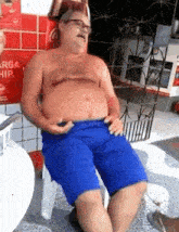 a shirtless man in blue shorts sits in a chair