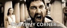 a man with a beard is screaming and saying `` this is my corner '' while a woman stands in the background .