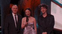 a man in a suit and tie stands next to a woman in a strapless dress and a man in a black suit .