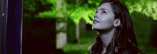 a woman is looking up at the sky while standing in front of a green forest .