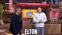 two men are standing next to each other in front of a sign that says elton on it .