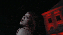 a woman with red hair is standing in front of a building with red lights on it
