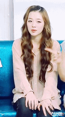 a woman with long hair is sitting on a couch with her hands folded in front of her