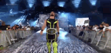 a wrestler in a black and green outfit is walking on a stage .