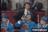 a man in a suit and tie is talking to a hockey player who is drinking from a green bottle .