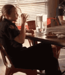 a woman in a police uniform sits at a table drinking from a mug