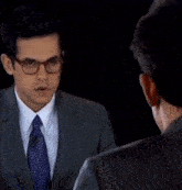 a man in a suit and tie talks to another man with glasses
