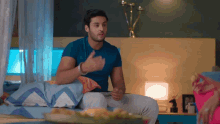 a man in a blue shirt is sitting on a bed talking
