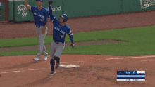 two blue jays baseball players on the field with a scoreboard in the background