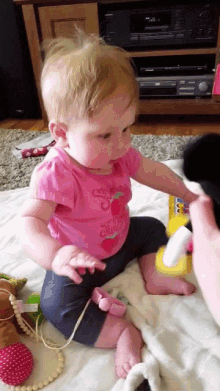 a baby in a pink shirt that says strawberry is playing with a toy
