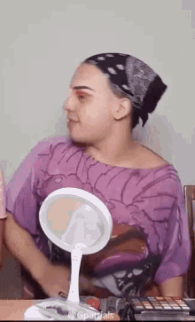 a woman wearing a purple shirt is sitting in front of a mirror .