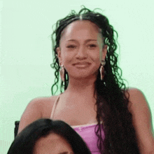 a woman with long curly hair and earrings is smiling while sitting next to another woman .