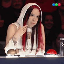 a woman with red and black hair sits at a table with a can that says got talent on it