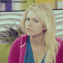a blonde woman wearing a pink hoodie and a blue shirt is looking at the camera