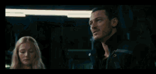 a man with his arms crossed looks at another man in a dark room